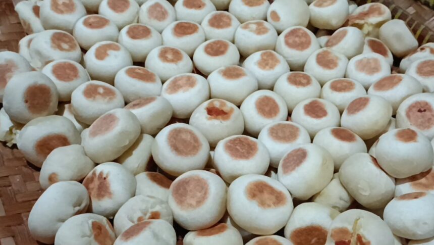 Pile of small white steamed buns with light brown tops in a basket.