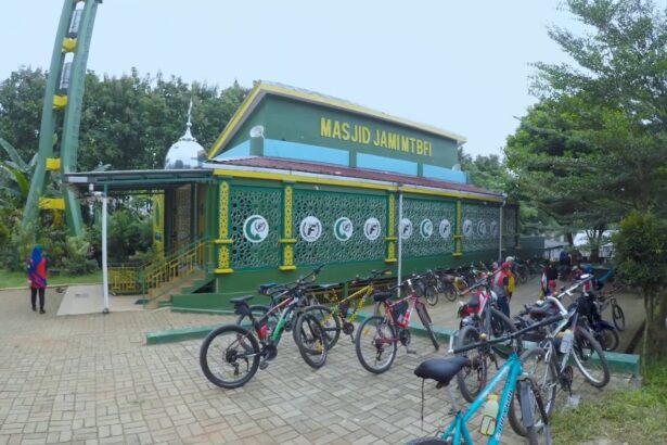 Green mosque with yellow trim and decorative lattice walls, named Masjid Jami MTBFI, and a row of bicycles parked outside with people nearby.