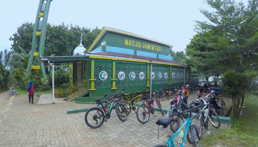 Green mosque with yellow trim and decorative lattice walls, named Masjid Jami MTBFI, and a row of bicycles parked outside with people nearby.