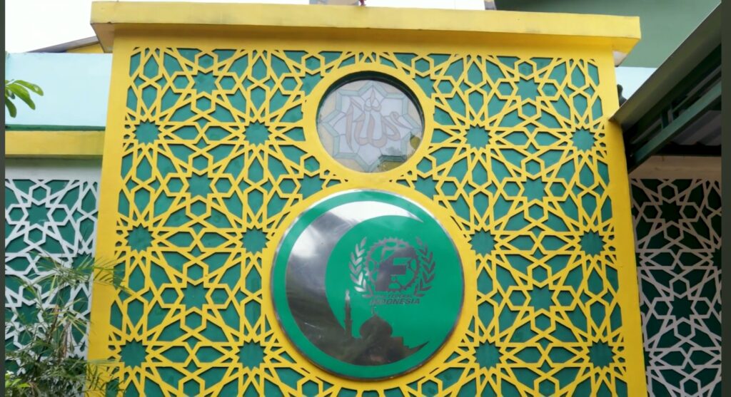 Decorative yellow lattice wall with geometric star patterns and a central green circular emblem, part of a colorful building façade.
