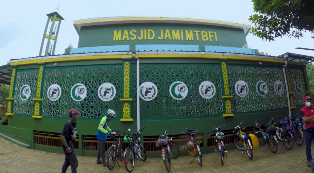 Exterior of Masjid JamimtbfI with a green lattice wall, yellow trim, and a line of bicycles parked along the entrance.