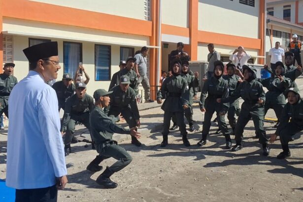 Group of uniformed trainees performing a martial arts drill outdoors, supervised by a man in a white coat and black hat, with onlookers in the background.