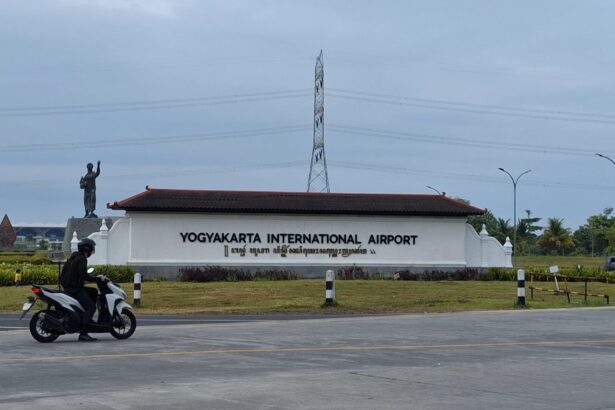 Yogyakarta International Airport sign with a statue to the left and a motorcyclist passing on the road in the foreground.