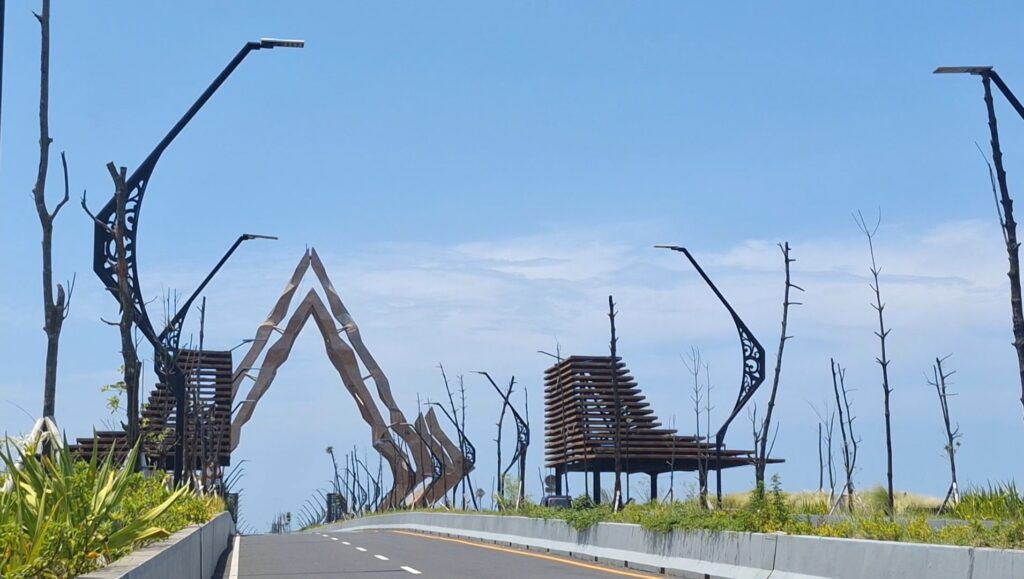 Wide view of a road with decorative black metal sculptures and leafless trees along a median under a clear blue sky