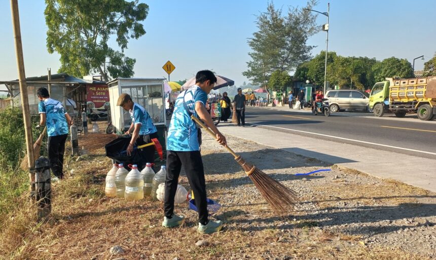 Three workers in blue uniforms sweep gravel along a roadside market area with water jugs and bags nearby