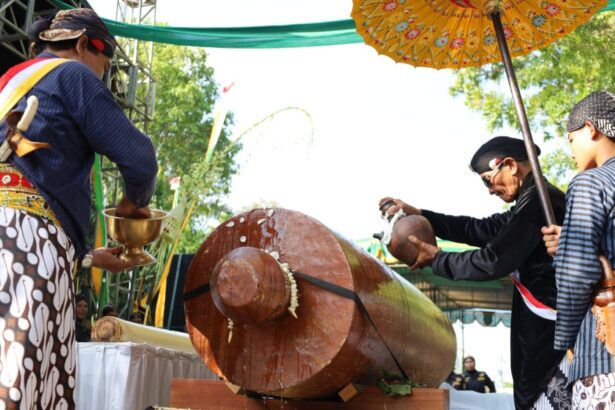 Group of people in traditional clothing performing a ceremonial drum beat on a large wooden drum.