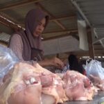 Woman wearing a hijab at an outdoor meat stall, handling large cuts of raw meat on a counter