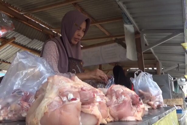 Woman wearing a hijab at an outdoor meat stall, handling large cuts of raw meat on a counter