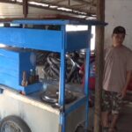 Street vendor beside a blue wooden cart with bottles on the counter, man in a cap and casual clothes nearby.
