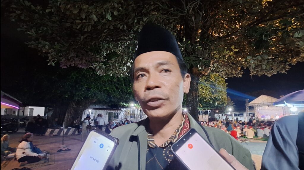 Screenshot_20260719_134653_Gallery - Mabur.co Uniformed man being interviewed at night as reporters hold up smartphones and microphones nearby; a crowd sits in the background under trees.