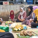 A group of women and a child sit cross‑legged on a mat in a circle, sharing food and drinks outdoors.