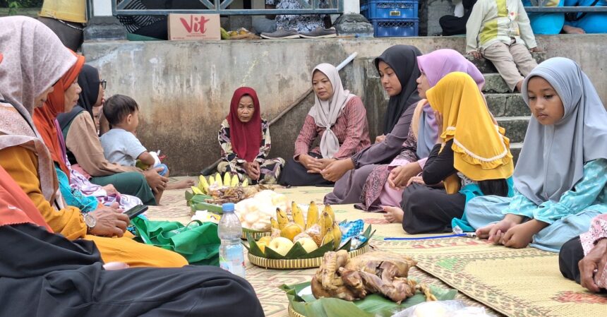 A group of women and a child sit cross‑legged on a mat in a circle, sharing food and drinks outdoors.