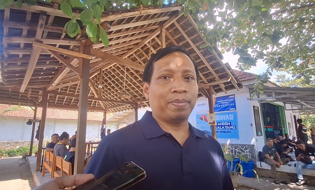 Screenshot_20260724_234649_Gallery - Mabur.co Smiling man in a dark polo shirt outdoors under a wooden pergola with people seated in the background and a blue poster on a wall behind him.