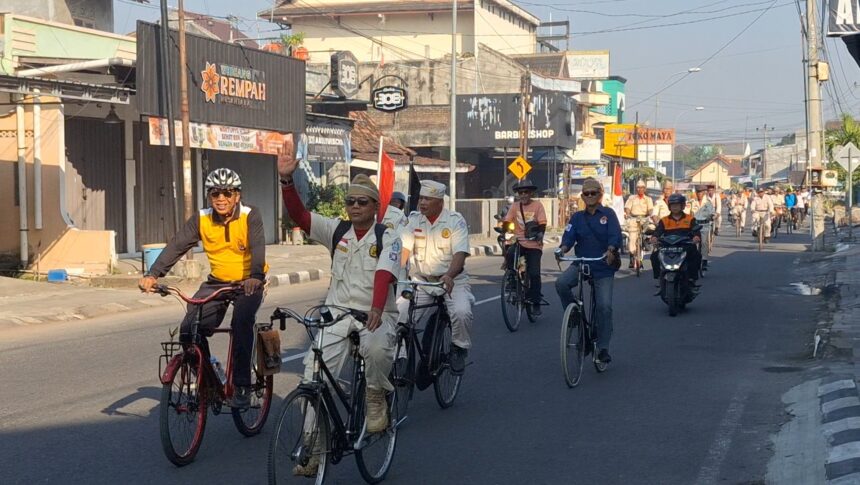 Group of cyclists riding down a city street during a parade, some in uniforms and waving flags