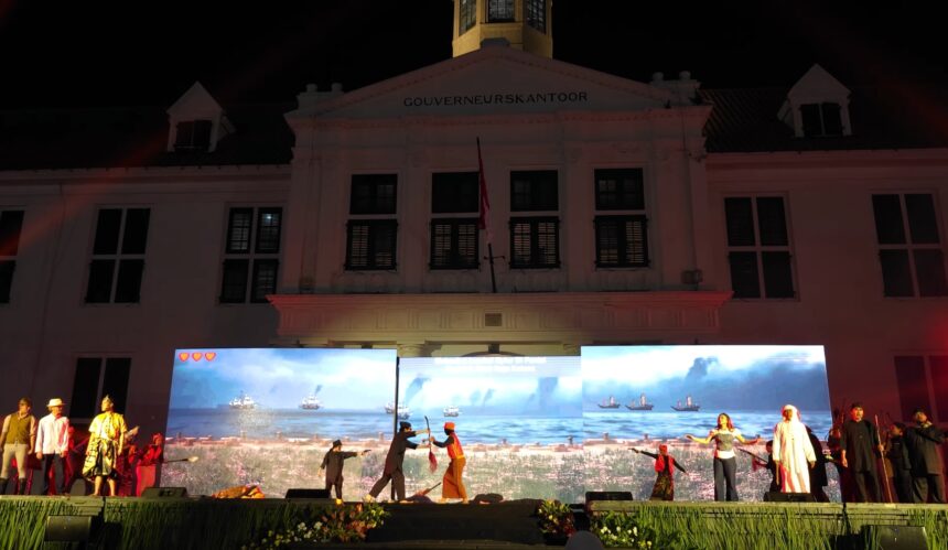 Nighttime stage performance in front of a white government building with 'GOUVERNEURSKANTOOR' on the facade and LED screens showing a seaside scene with ships.