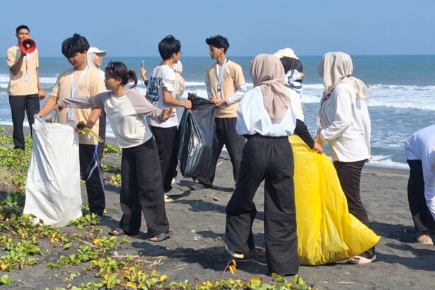 Group of volunteers on a beach collecting litter, passing filled bags toward a central pile by the sea.