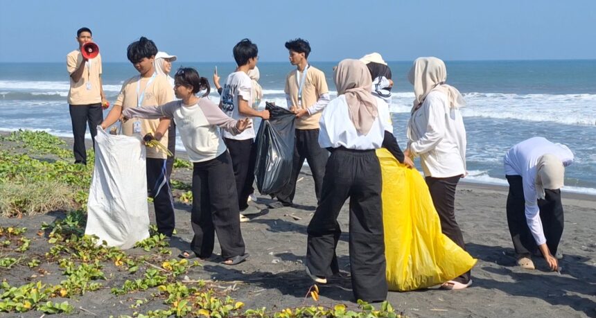 Group of volunteers on a beach collecting litter, passing filled bags toward a central pile by the sea.