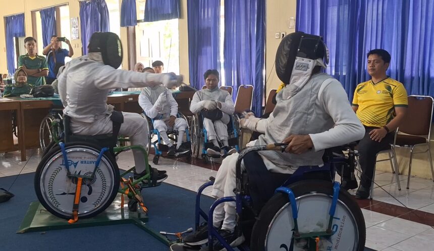 Wheelchair fencers in full protective gear and masks compete in an indoor demo, with spectators watching behind blue curtains.