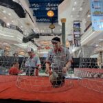 Indoor mall atrium with multiple wire chicken cages on a red carpet, people moving around a poultry exhibit.