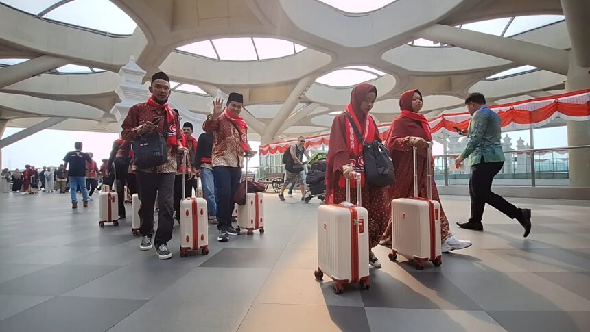 Group of travelers in red traditional outfits with rolling white suitcases in a modern airport terminal with a sculpted ceiling.