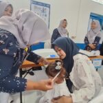 Women in hijabs assist a young girl in a clinic, performing a health check or procedure while others observe in the background.