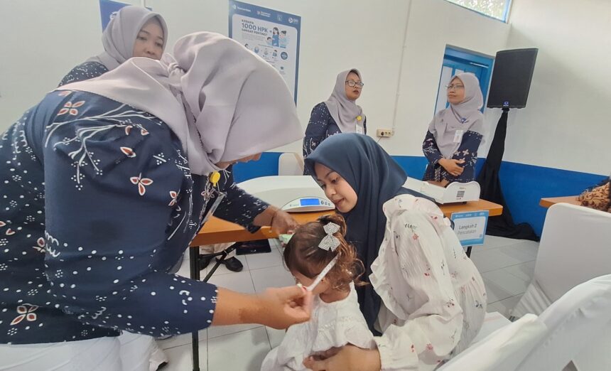 Women in hijabs assist a young girl in a clinic, performing a health check or procedure while others observe in the background.