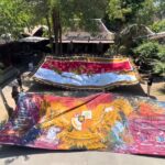 A group of people unfurling large, colorful banners in a shaded courtyard. Nicely painted maps and patterns span the fabric as they lay it out to display.