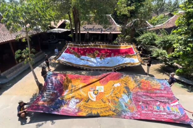 A group of people unfurling large, colorful banners in a shaded courtyard. Nicely painted maps and patterns span the fabric as they lay it out to display.