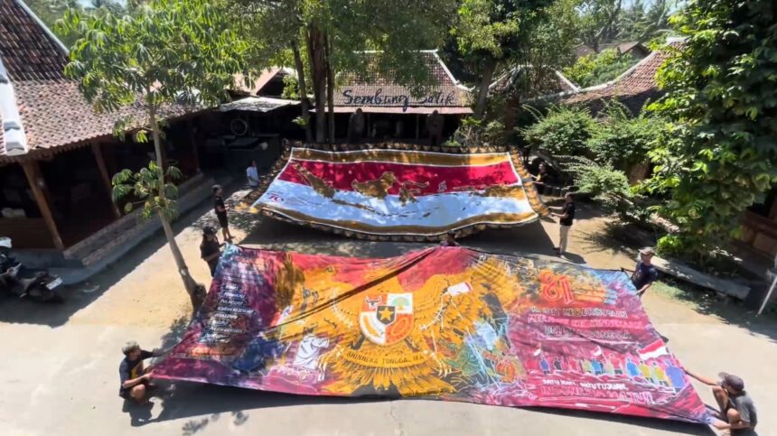 A group of people unfurling large, colorful banners in a shaded courtyard. Nicely painted maps and patterns span the fabric as they lay it out to display.