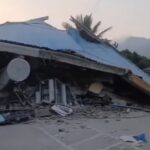 Collapsed structure with a blue metal roof, rubble strewn across the ground and a satellite dish in the foreground