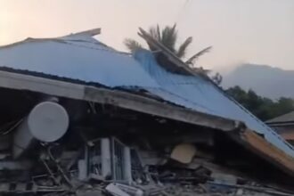 Collapsed structure with a blue metal roof, rubble strewn across the ground and a satellite dish in the foreground