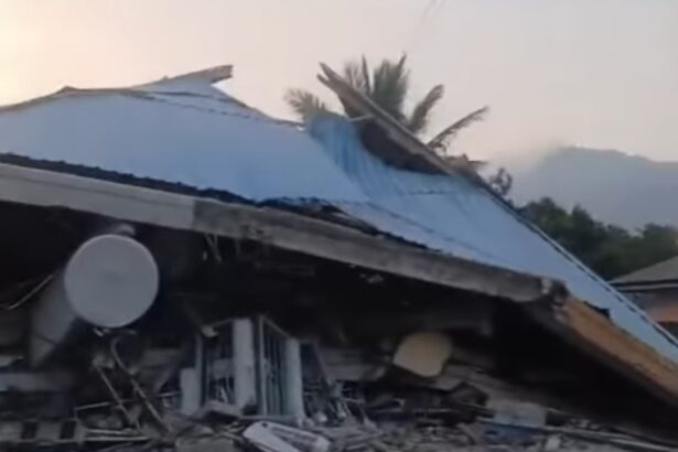 Collapsed structure with a blue metal roof, rubble strewn across the ground and a satellite dish in the foreground