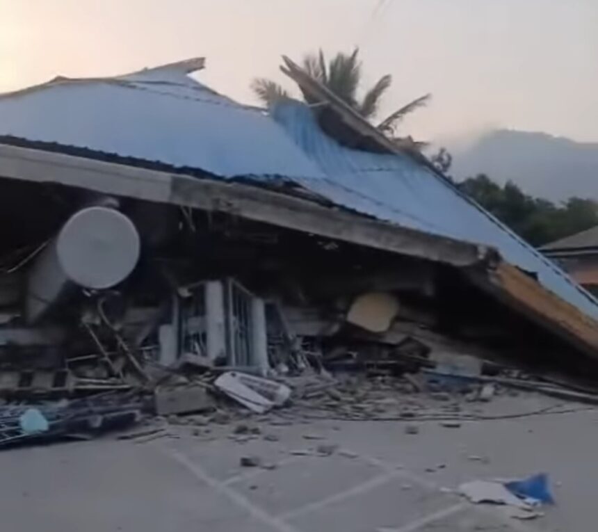 Collapsed structure with a blue metal roof, rubble strewn across the ground and a satellite dish in the foreground