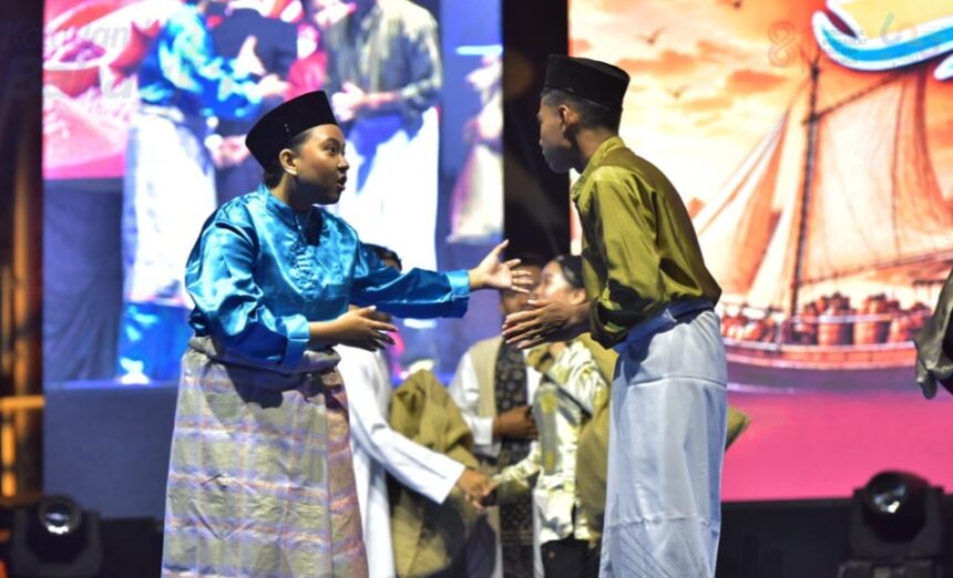 Two men in traditional Malay attire greet each other with a handshake on stage during a cultural performance, with a colorful backdrop behind them.