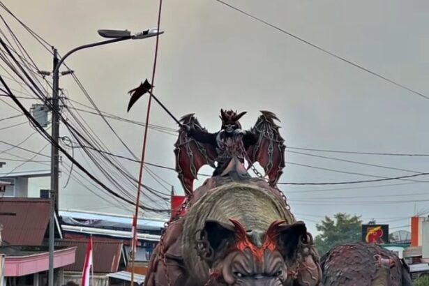 Large demon-like float with a dragon on its back in a street parade, crowds watching along the street.