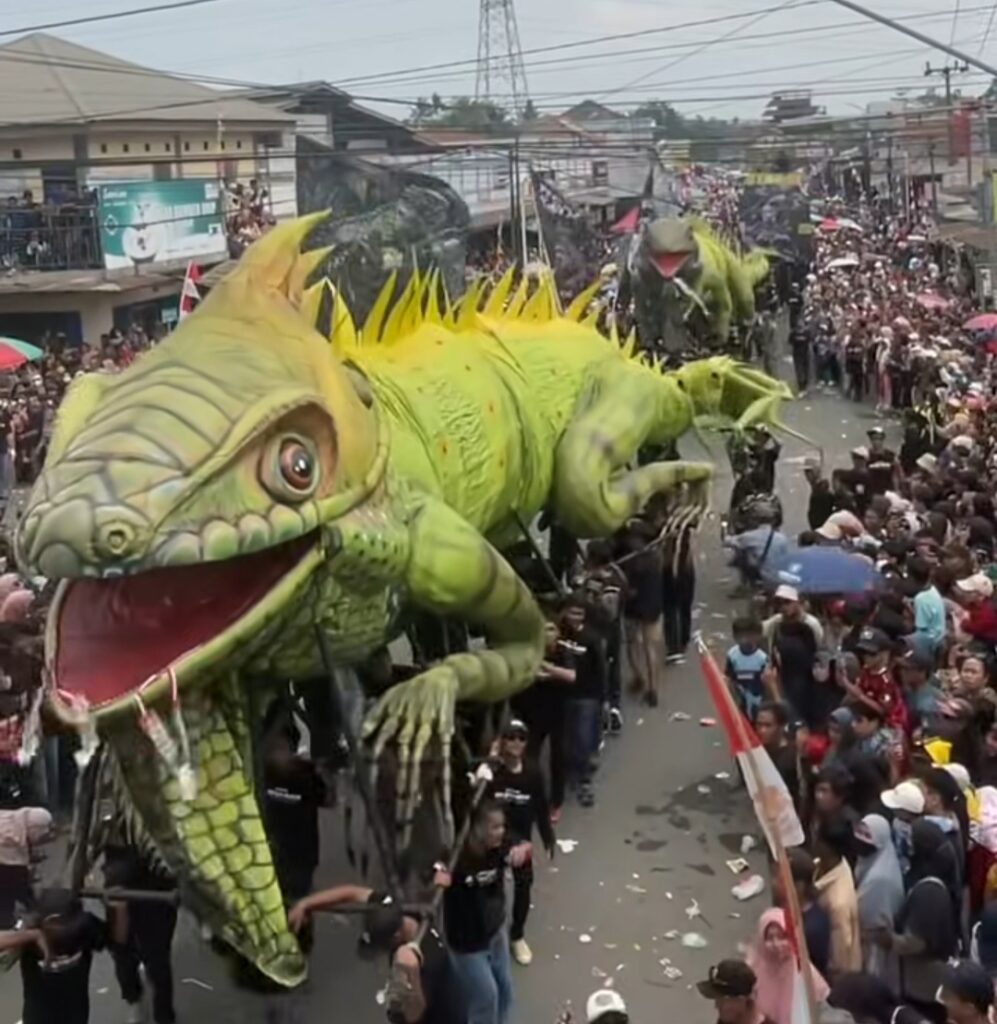 Screenshot_20260818_124613_Instagram - Mabur.co Large green dragon float with spiky yellow dorsal fins parades through a crowded street, spectators on both sides cheering and taking photos.