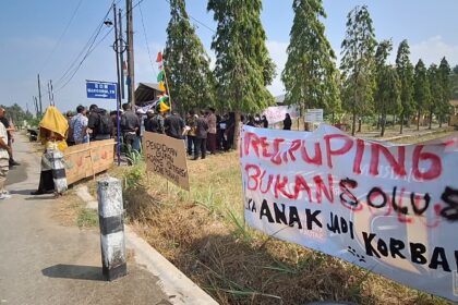 Group of people protesting along a rural road with banners and signs under a blue sky.