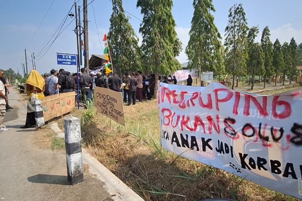 Group of people protesting along a rural road with banners and signs under a blue sky.