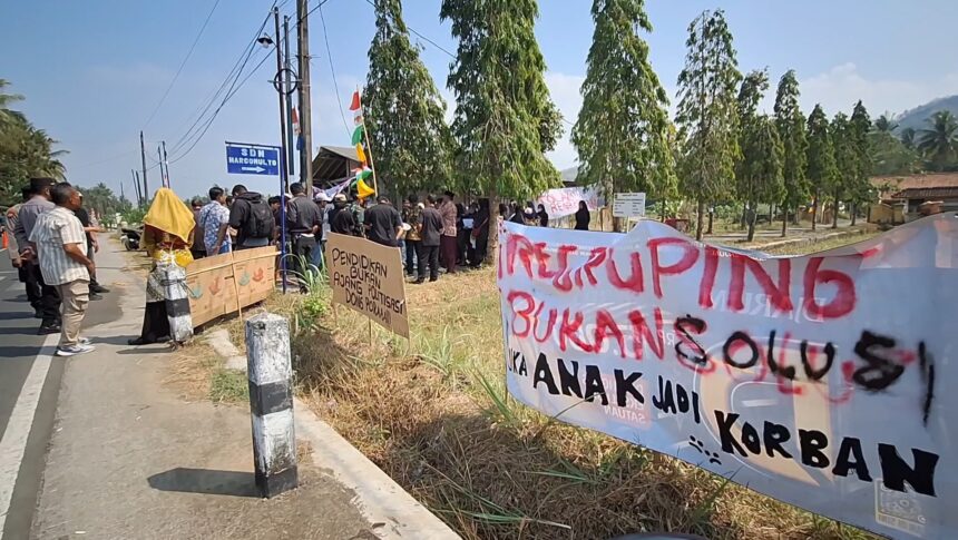 Group of people protesting along a rural road with banners and signs under a blue sky.