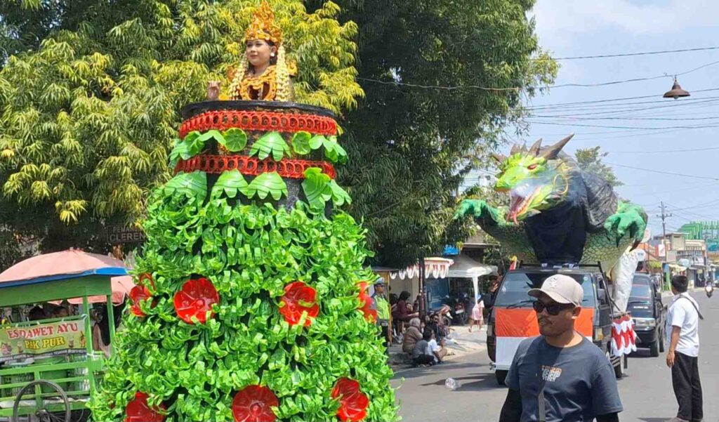 Colorful dragon parade float with a rider wearing a floral headdress perched on top, green body with red accents moving through a street crowd.