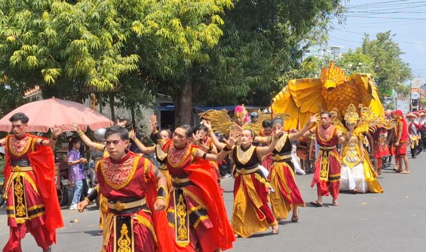 Dancers in red and gold costumes perform a street parade, followed by a large yellow phoenix float with golden decorations in the background.