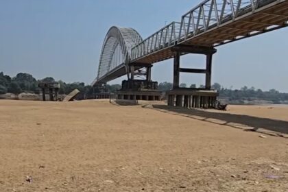 Steel arch/Truss bridge spanning a dry, sandy riverbed with concrete supports in the distance