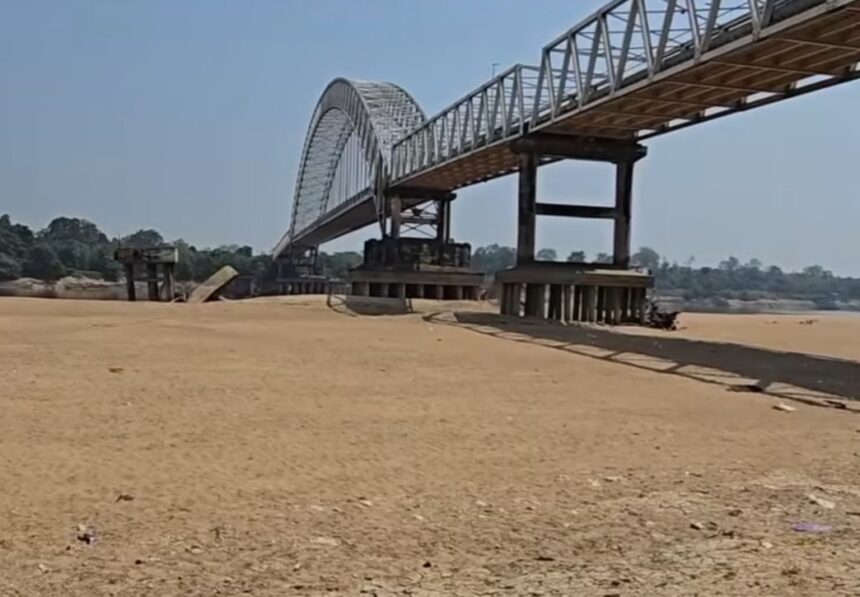 Steel arch/Truss bridge spanning a dry, sandy riverbed with concrete supports in the distance