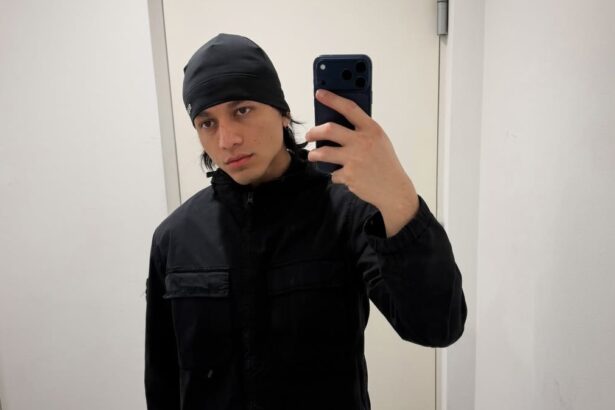Young man in a black beanie and jacket taking a mirror selfie with a dark smartphone.