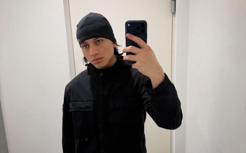 Young man in a black beanie and jacket taking a mirror selfie with a dark smartphone.