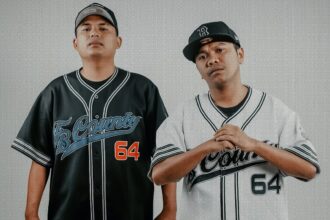 Two men in matching baseball-style jerseys stand side by side, one in black and the other in white, with bold orange text 'NDX AKA' across the bottom.
