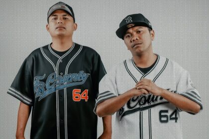 Two men in matching baseball-style jerseys stand side by side, one in black and the other in white, with bold orange text 'NDX AKA' across the bottom.