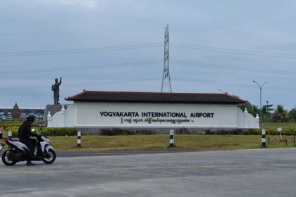 Entrance sign for Yogyakarta International Airport with a statue on the left and a motorcyclist on the road in the foreground.