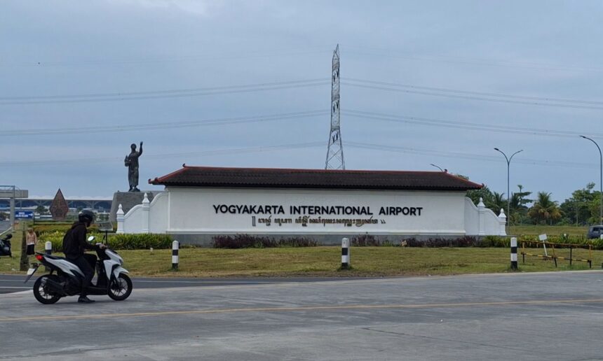 Entrance sign for Yogyakarta International Airport with a statue on the left and a motorcyclist on the road in the foreground.