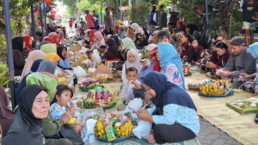 Screenshot_20260907_121154_Gallery - Mabur.co Large group of people sitting on mats in a park, sharing snacks and bananas during a communal charity event in progress.